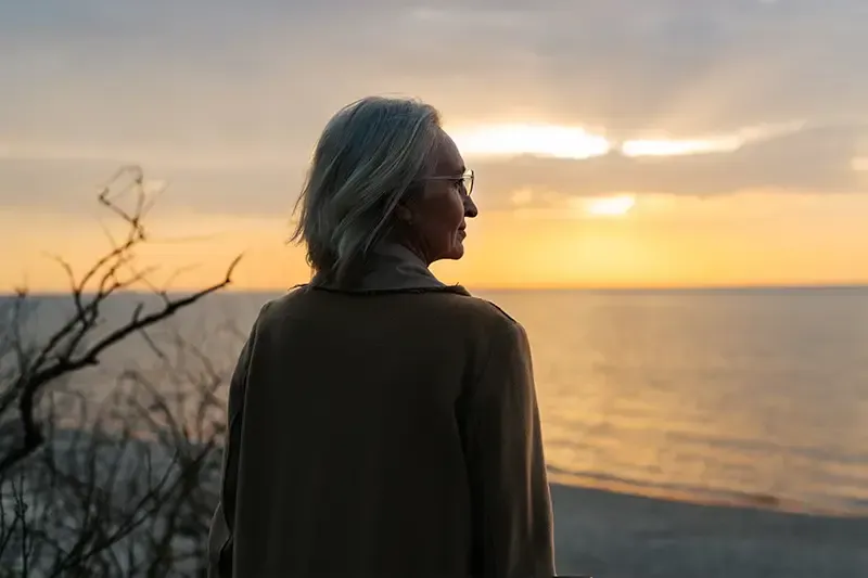 A woman gazes off into the sunset as she contemplates the mental health concerns of older caregivers