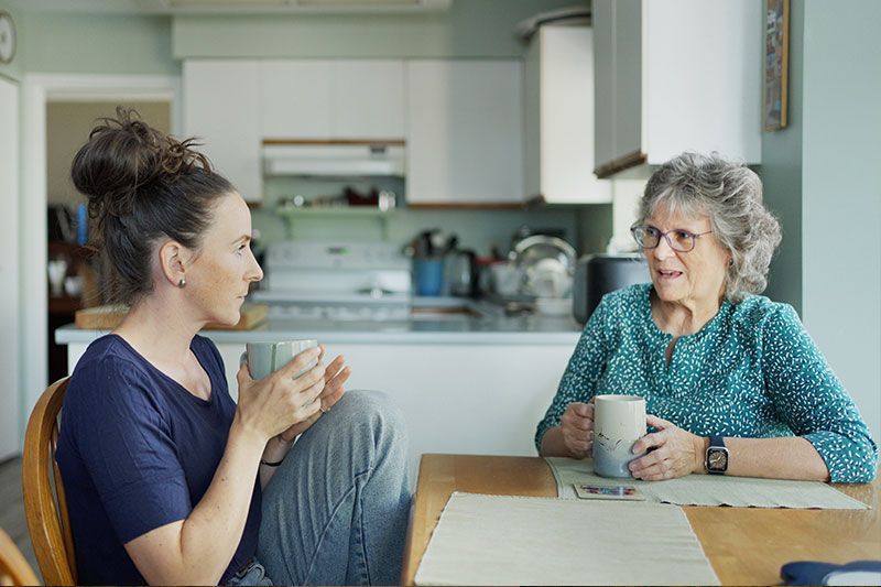 A woman experiencing the communication challenges of Alzheimer’s sits at the table with her daughter as they use unique strategies to connect.
