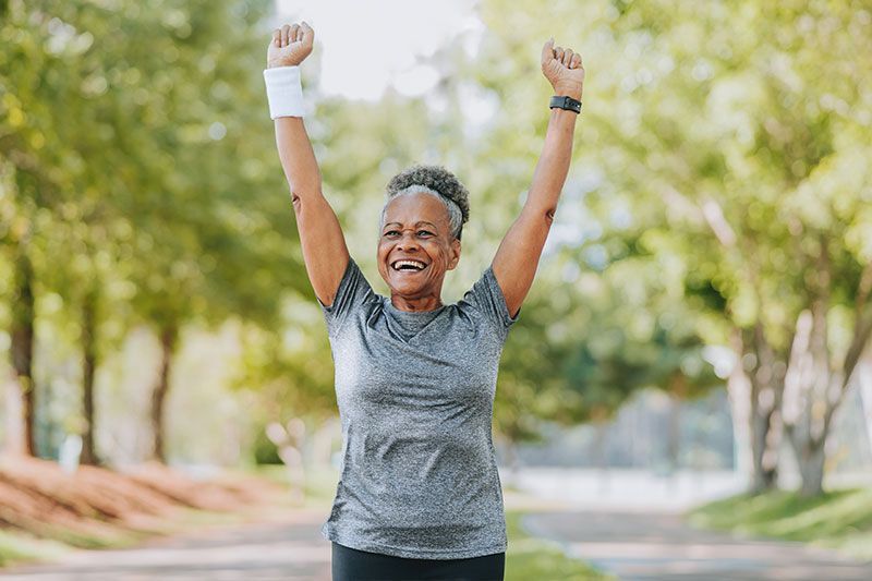 A family learned how to help a senior loved one set new goals, and as a result, an older woman raises her arms triumphantly to celebrate achieving one of those goals.