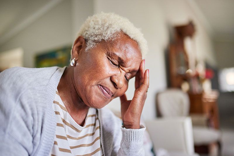 An older woman who struggles with COPD headaches winces as she touches her forehead.
