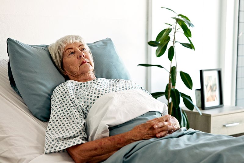 A woman lies in bed as she ponders what to do when short-term rehab extends into long-term care.
