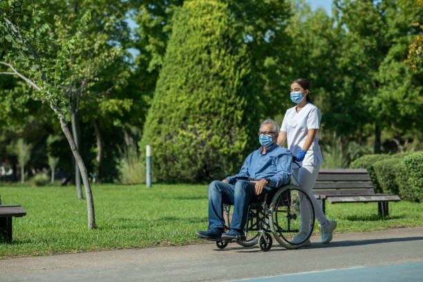 An older man enjoys a ride through the park in his wheelchair from his Boston respite care professional.