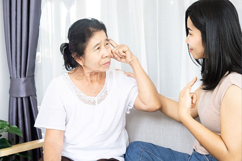 An older woman looks confused as her granddaughter points to herself, displaying the common scenario when someone with dementia forgets you.