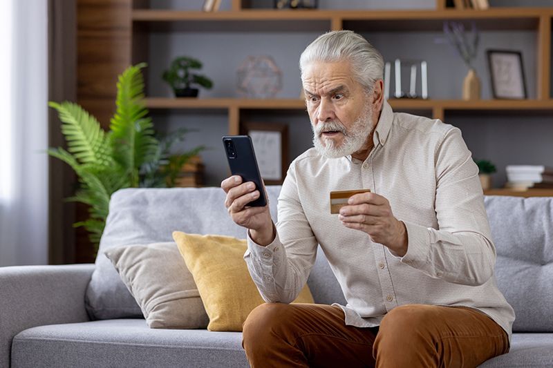 An older man looks alarmed as he sees a message on his phone that says, “Your account has been hacked!”