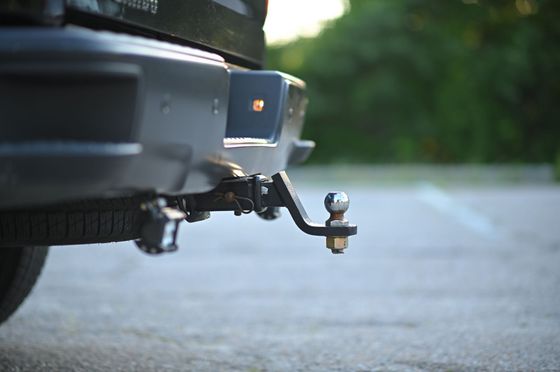 Close-up of a vehicle’s trailer hitch and tow ball in a parking area.