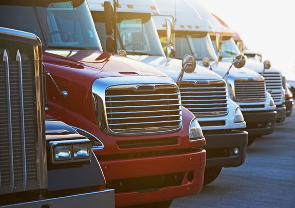 Parked semi-trucks lined up in a row, focusing on their front grills