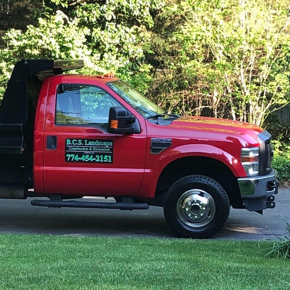 Red landscaping truck with business logo parked on grass.
