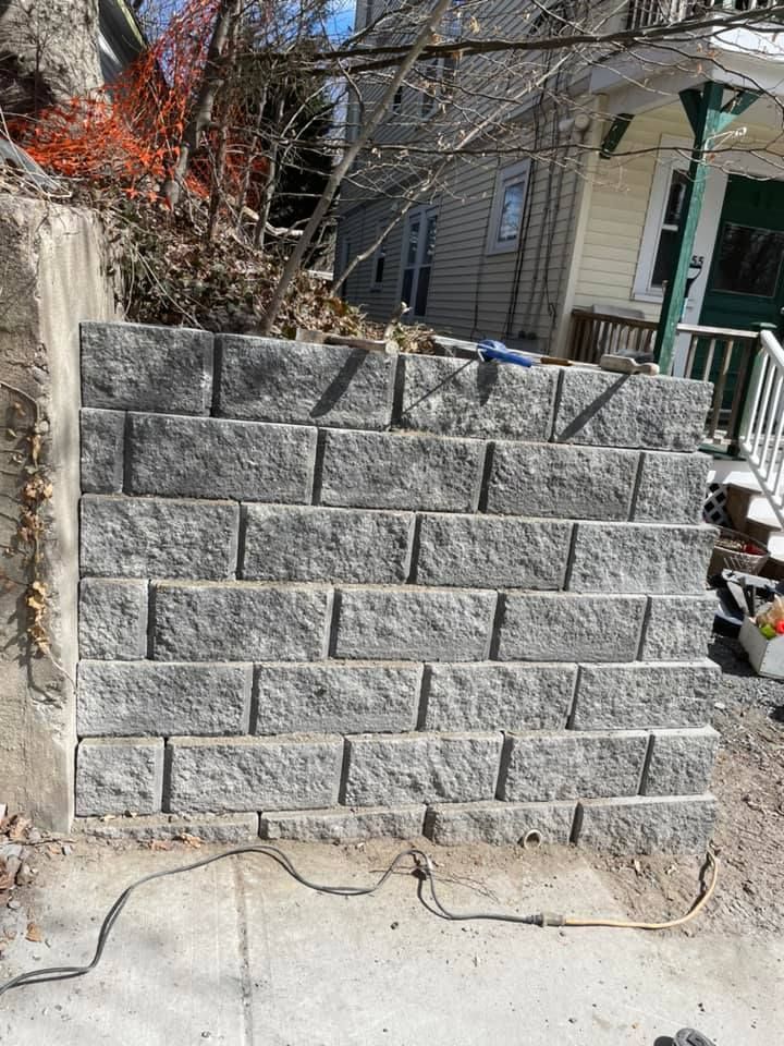 Gray retaining wall made of rectangular blocks, in front of a house.