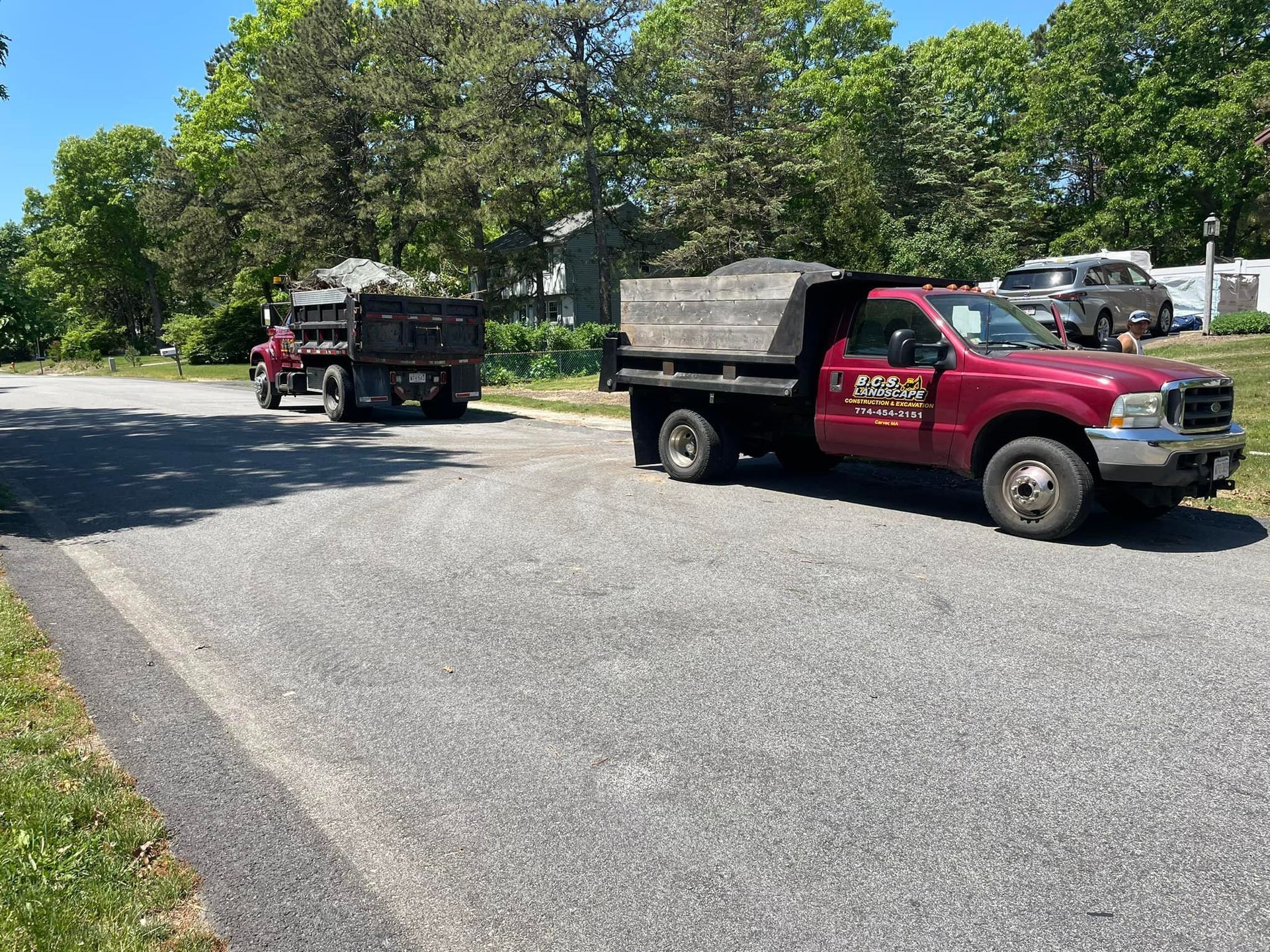 Two maroon dump trucks parked on a street, filled with debris. Sunny day.