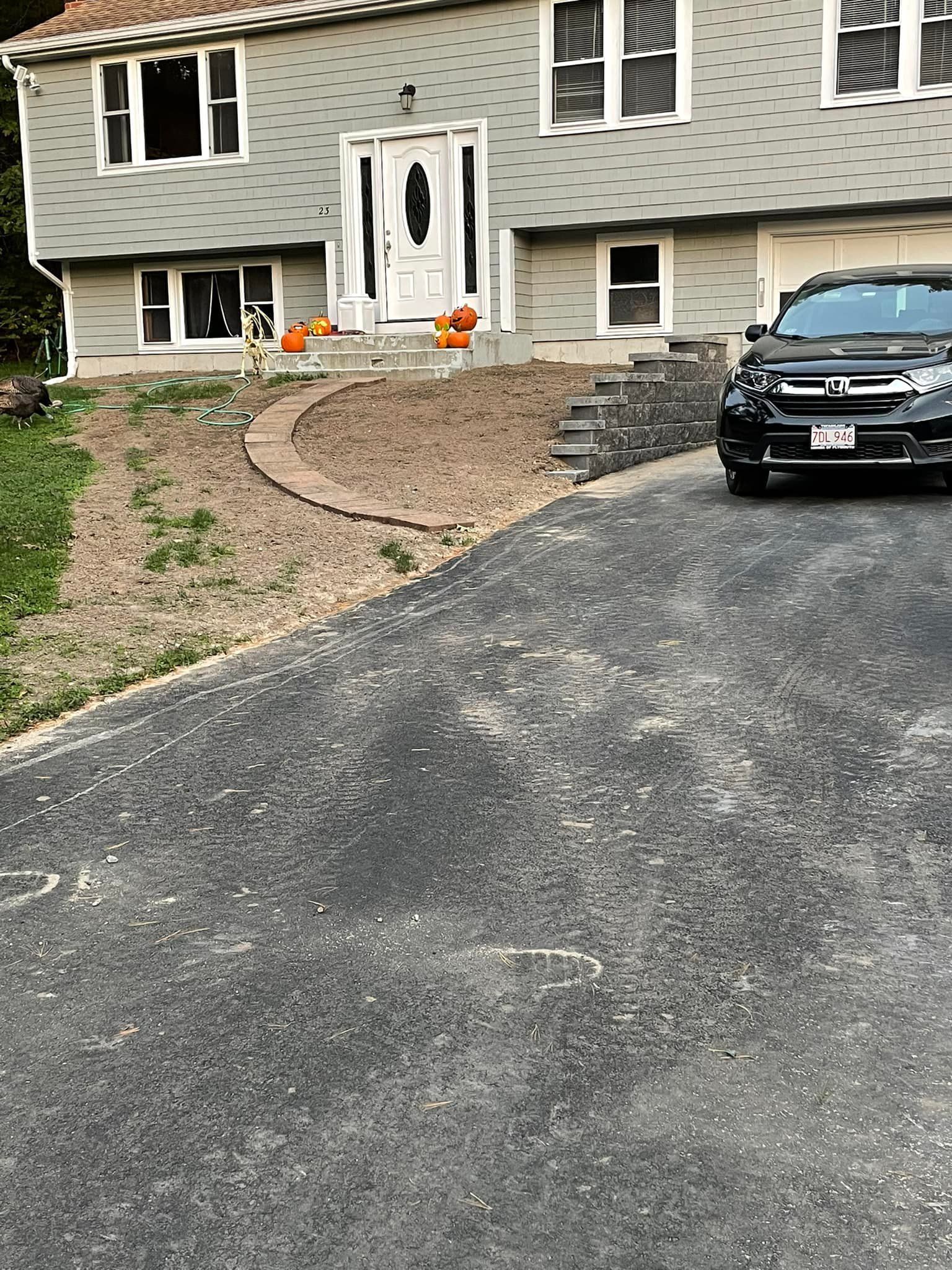 Gray house with a dark driveway and retaining wall. A black SUV is parked in front.