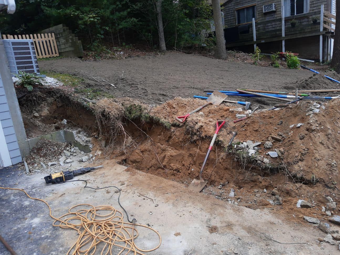 Excavation work in progress next to a driveway; soil and tools visible, with a house in the background.
