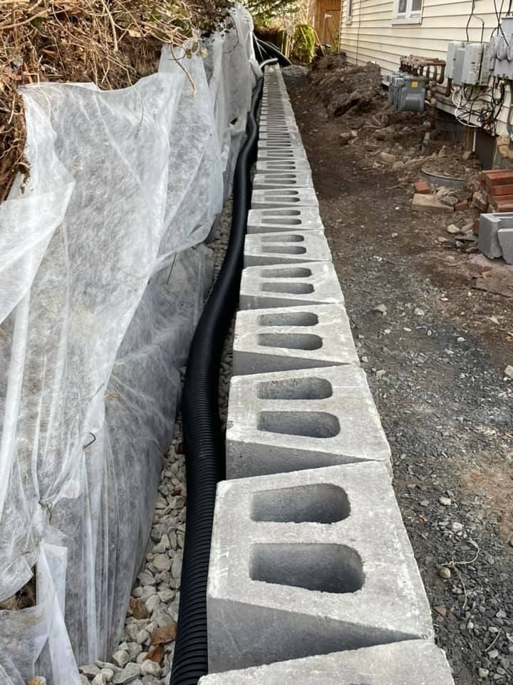 Retaining wall construction: concrete blocks, drainage pipe, and fabric lining a slope.