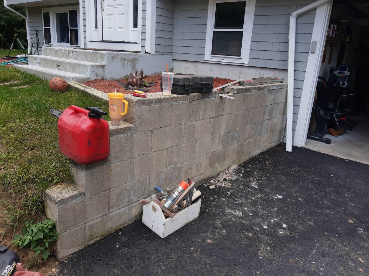 Exterior of a house with a cinder block wall, a red gas can, and a toolbox on the driveway.