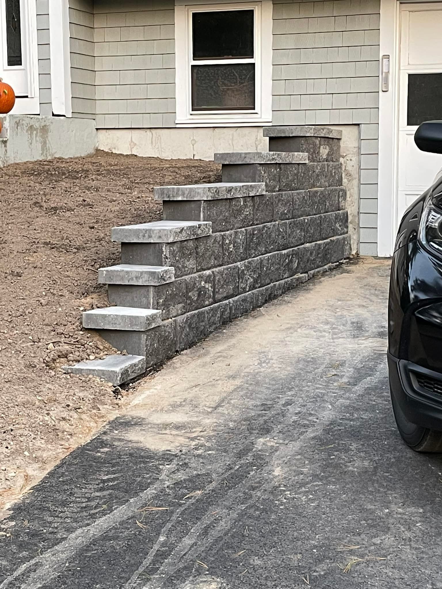 Stone retaining wall with steps, next to a garage and house with a window.