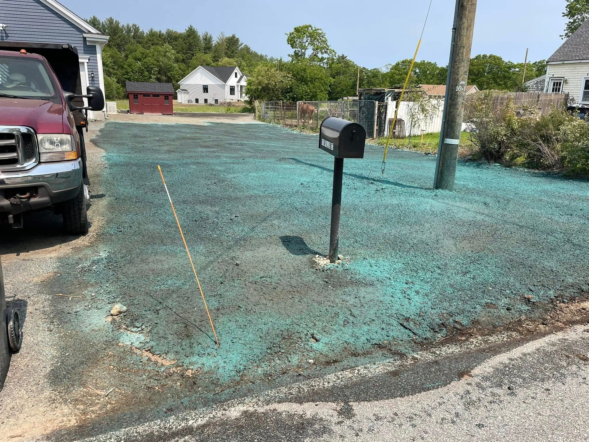 Lawn with blue-green seed covering, mailbox, utility pole, and parked truck on a sunny day in front of houses.