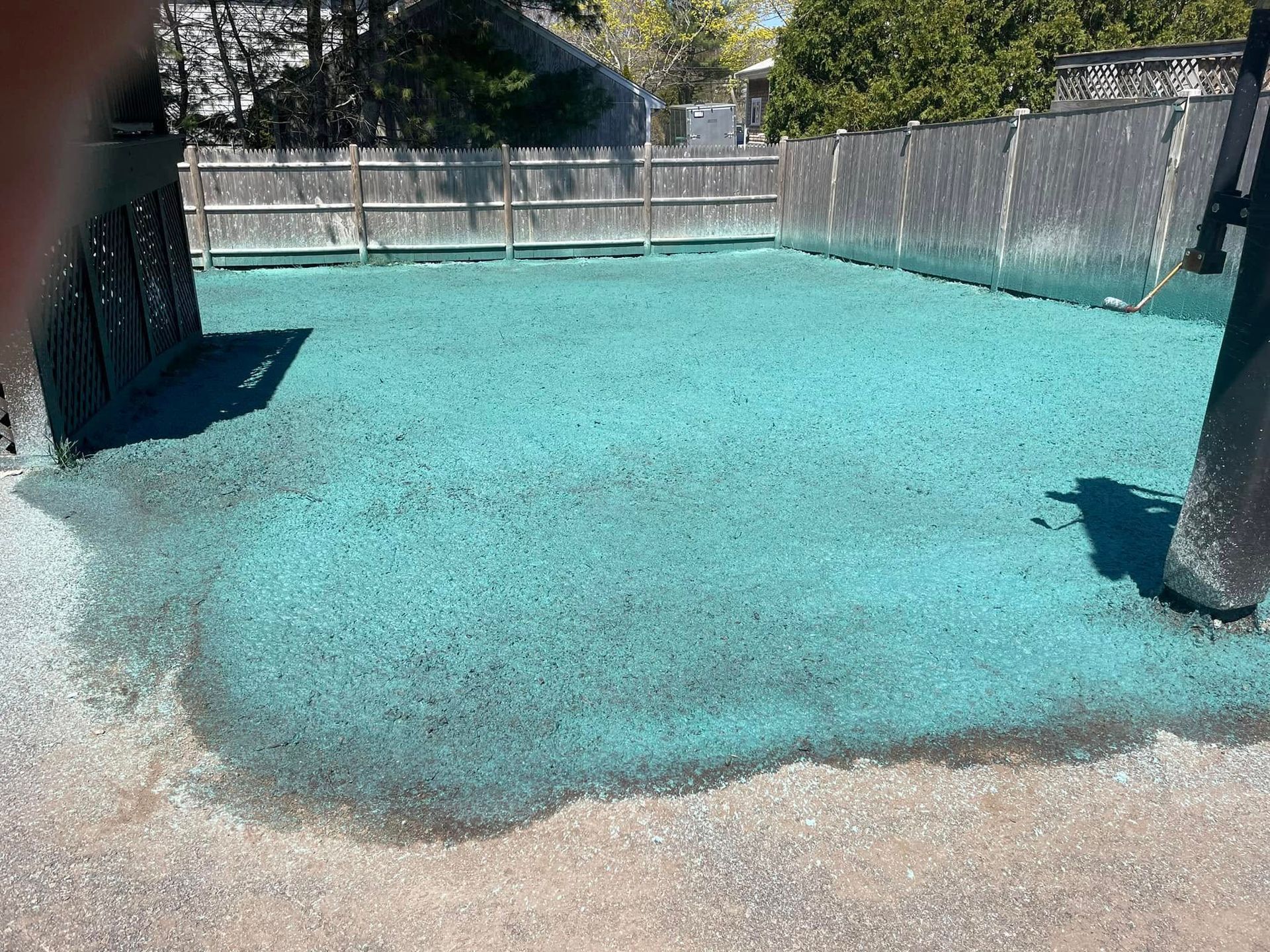 A ground area covered in bright blue material surrounded by a fence and a building.