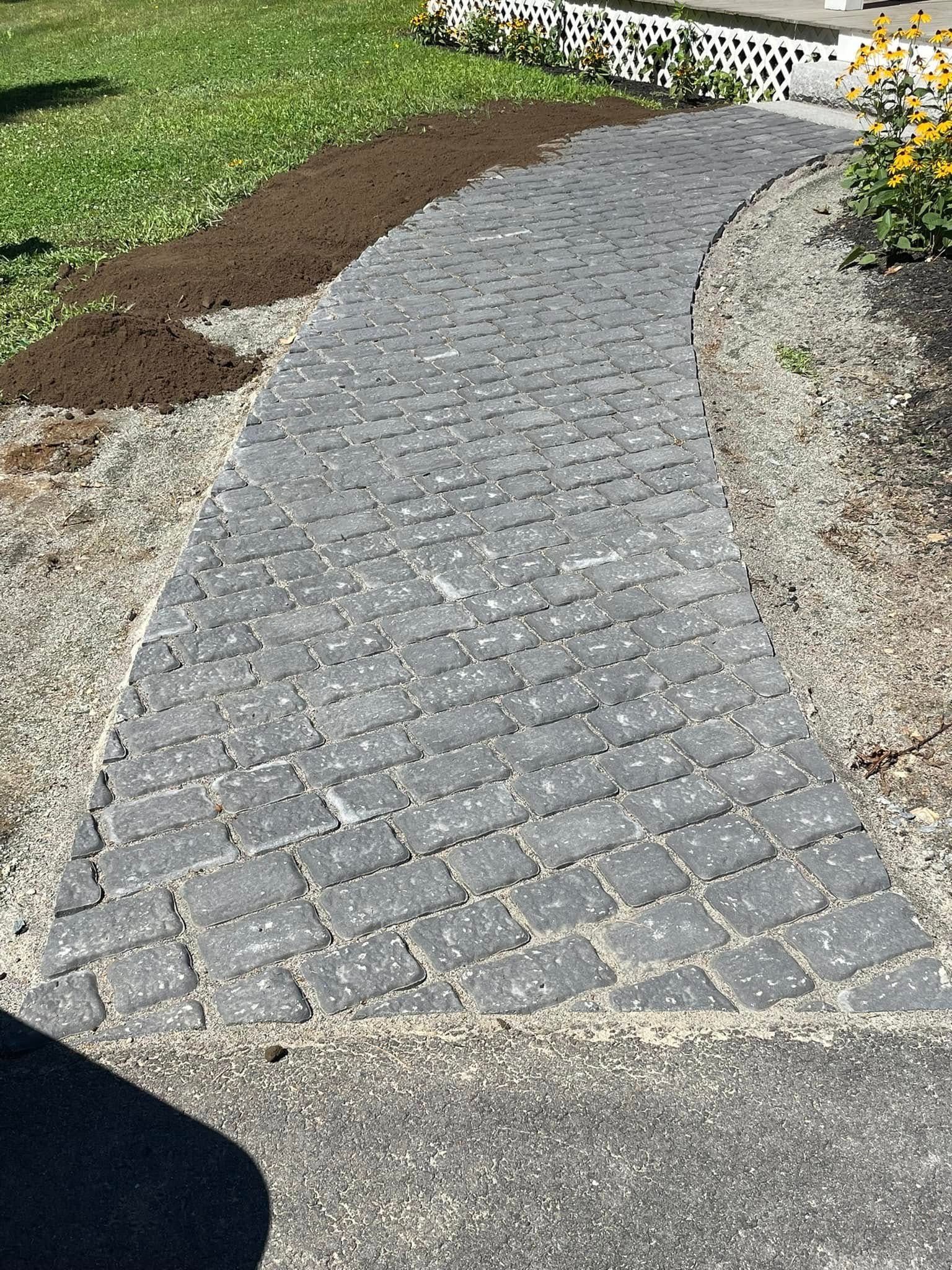 Brick walkway curving through a yard; soil on one side, gravel on the other.