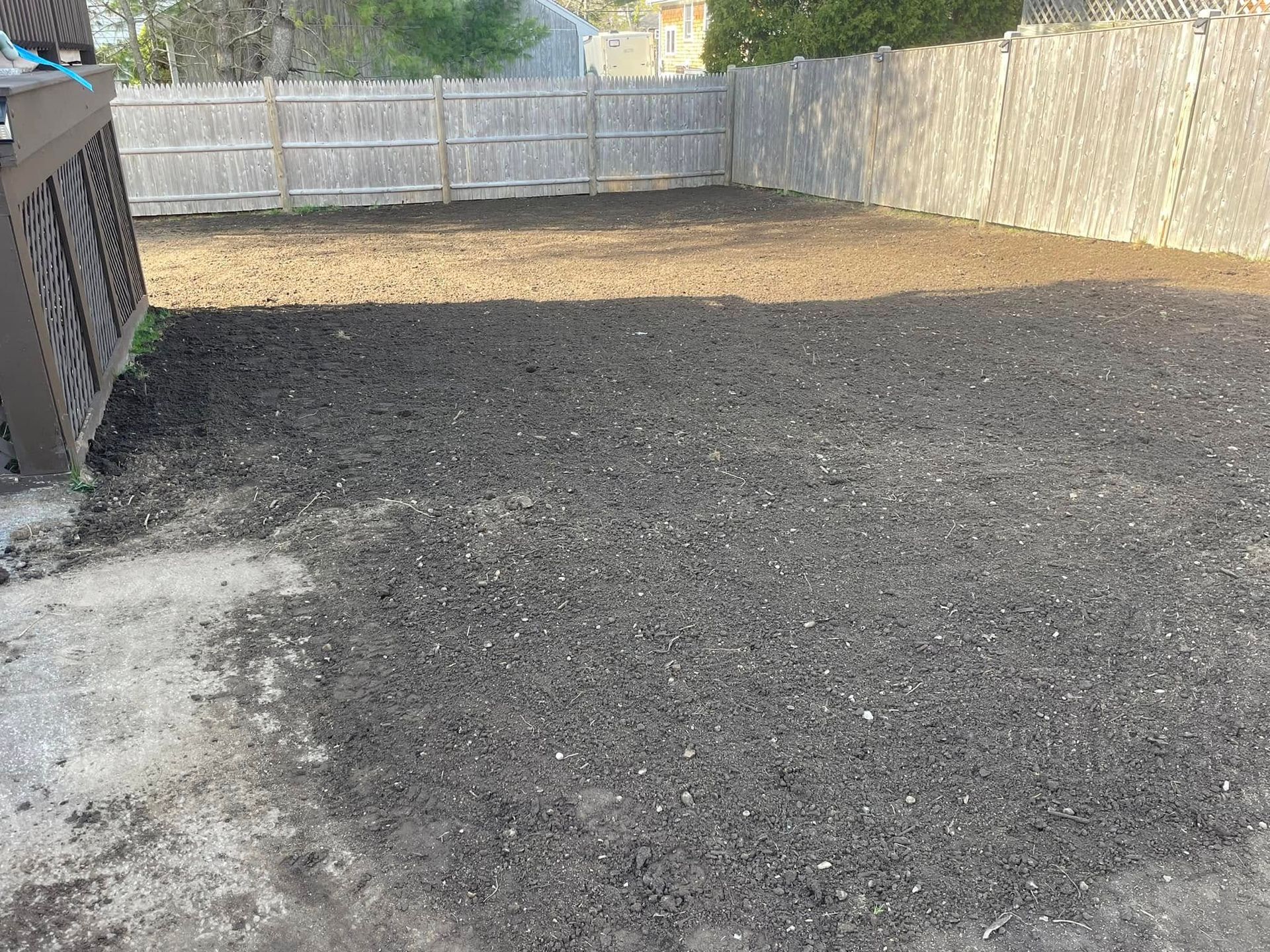 A backyard with dark soil, enclosed by a wooden fence and deck.