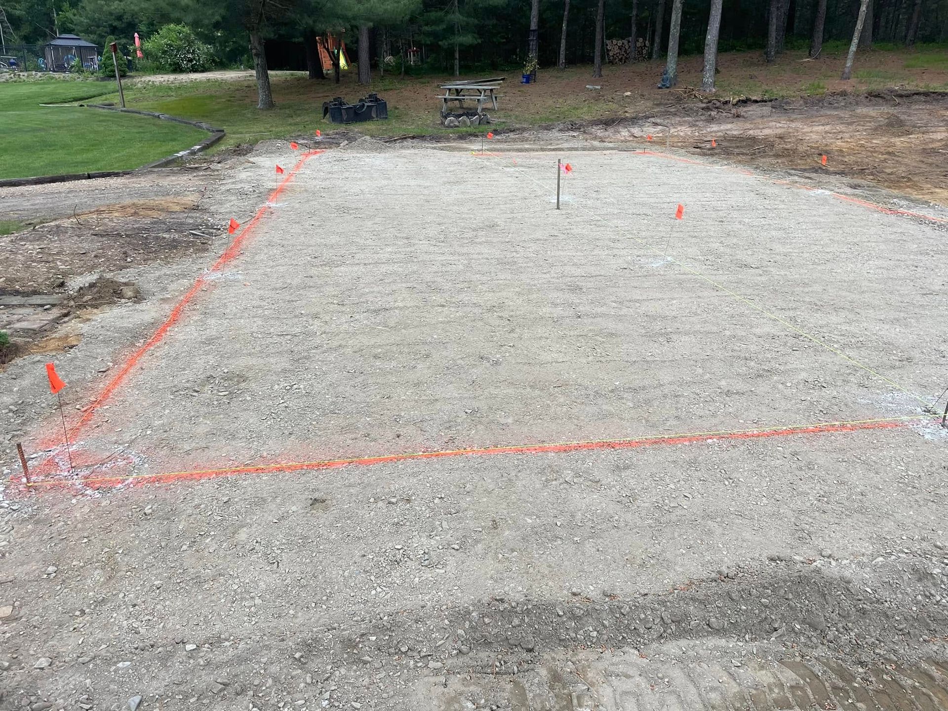 Gravel-covered, rectangular construction site outlined with orange spray paint, marked with small orange flags, outdoors.
