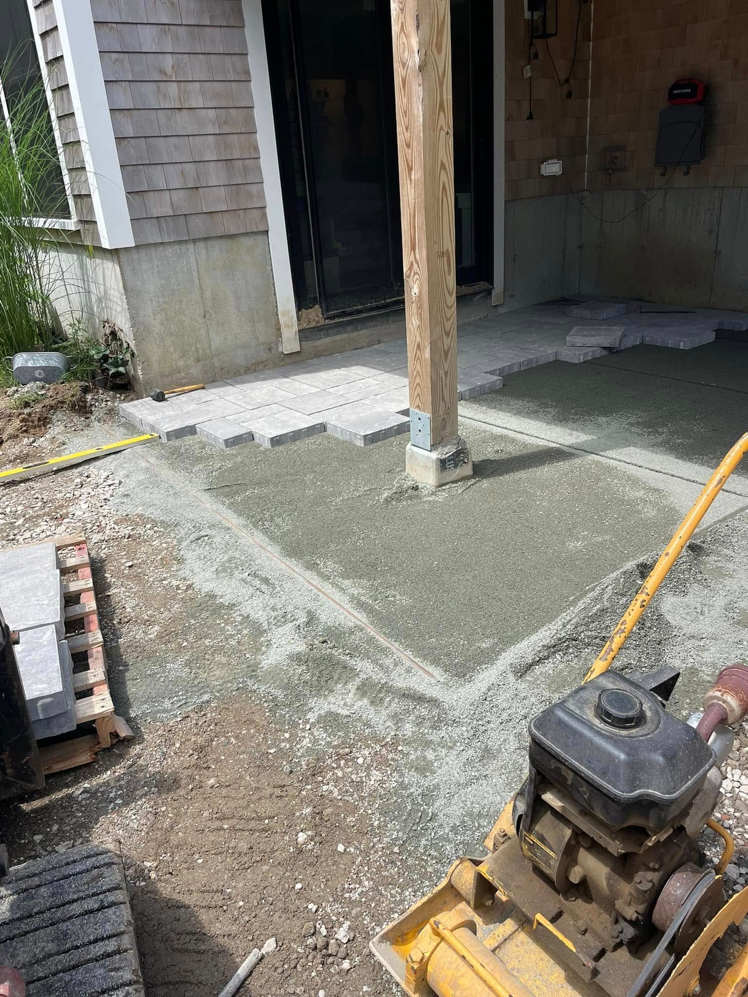 Construction site: Gravel base around a wooden post, pavers, and a compaction machine.
