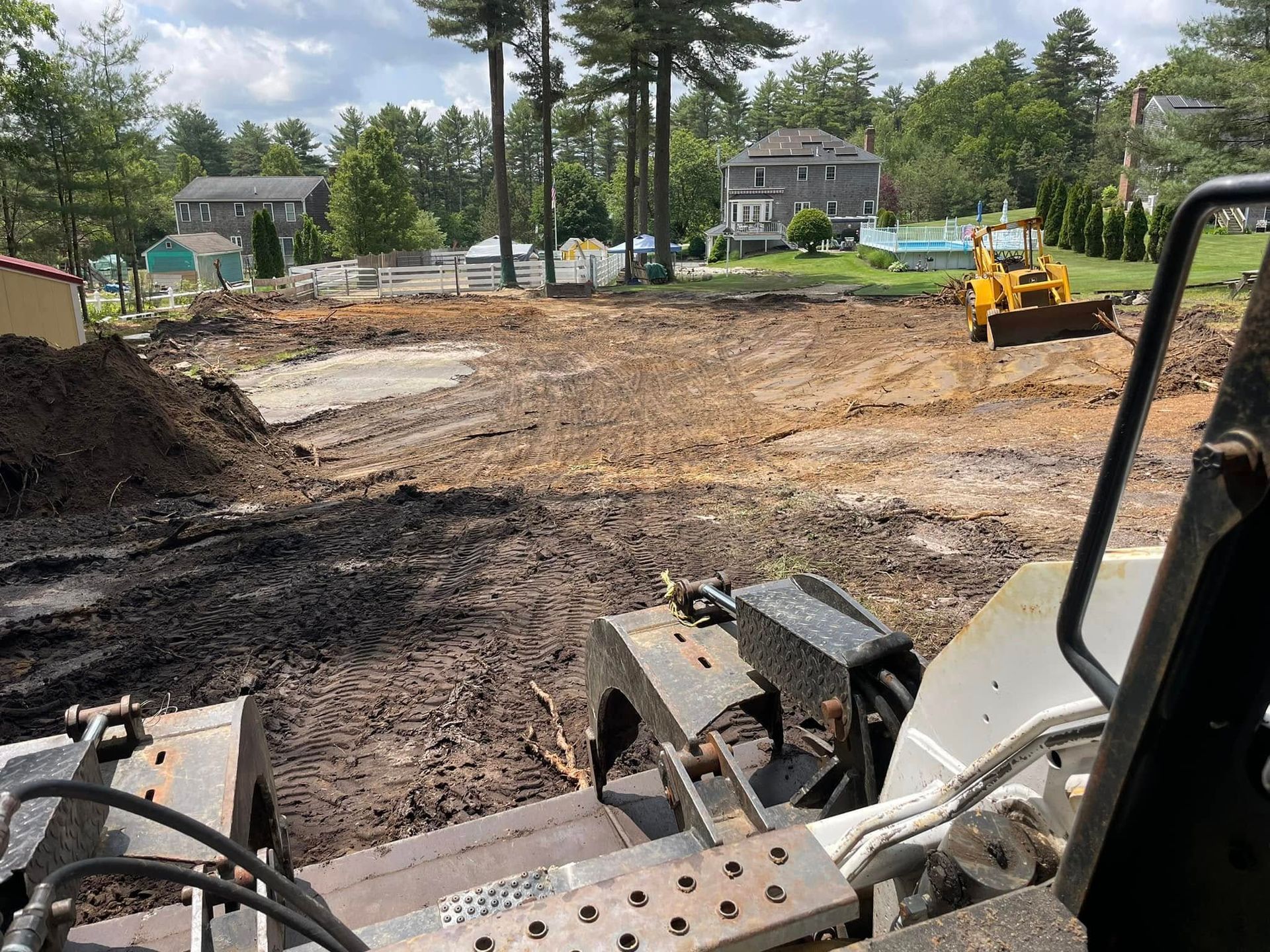 Construction site with dirt and heavy equipment, houses in background.