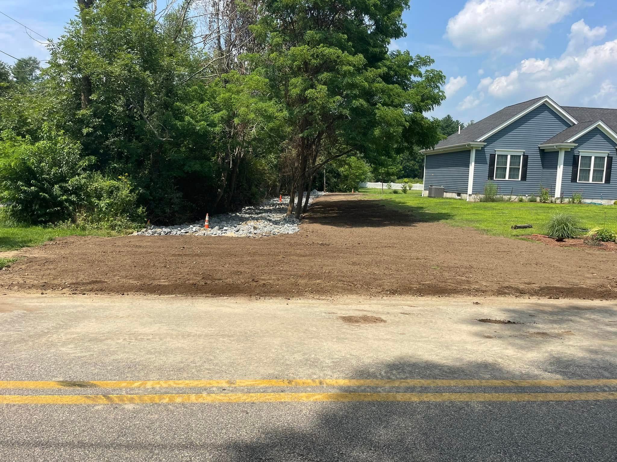 A newly planted bed of brown earth next to a road, with a blue house in the background.