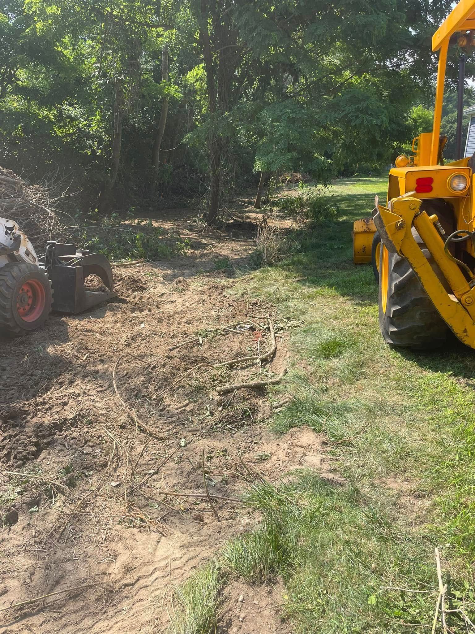 A Bobcat skid steer and yellow tractor working on a dirt area with brush. Sunlight.