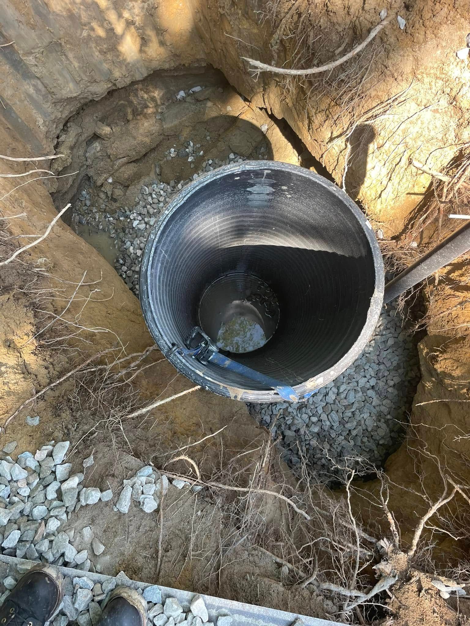 Black corrugated pipe in a dirt trench, surrounded by gravel, appears to be an opening to a well or drainage system.