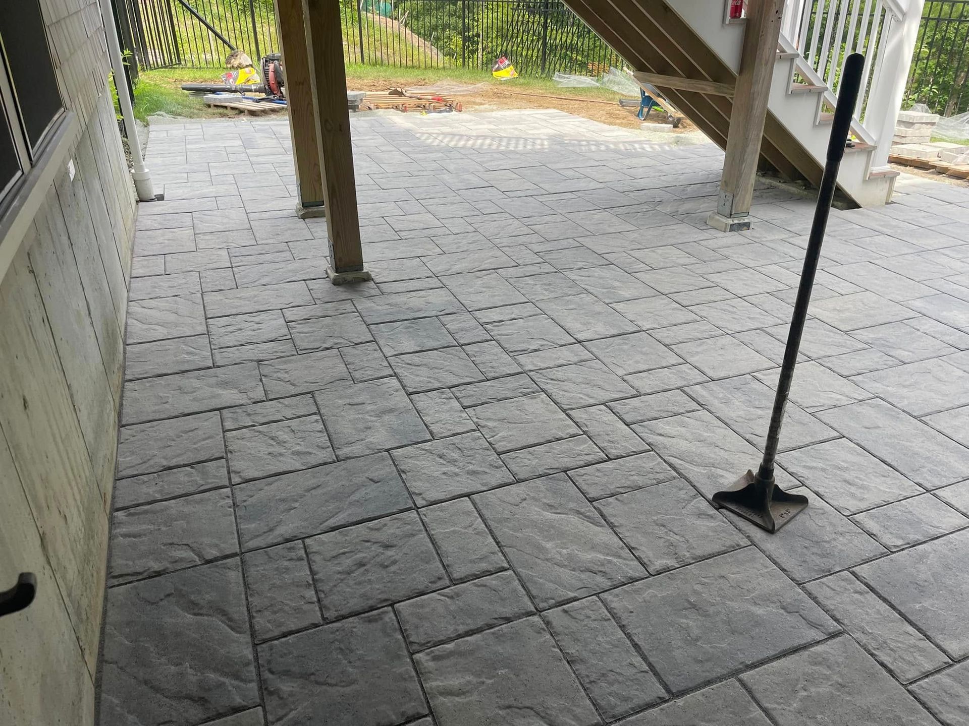 Gray pavers on a patio under a deck. A compactor tool rests on the pavers.