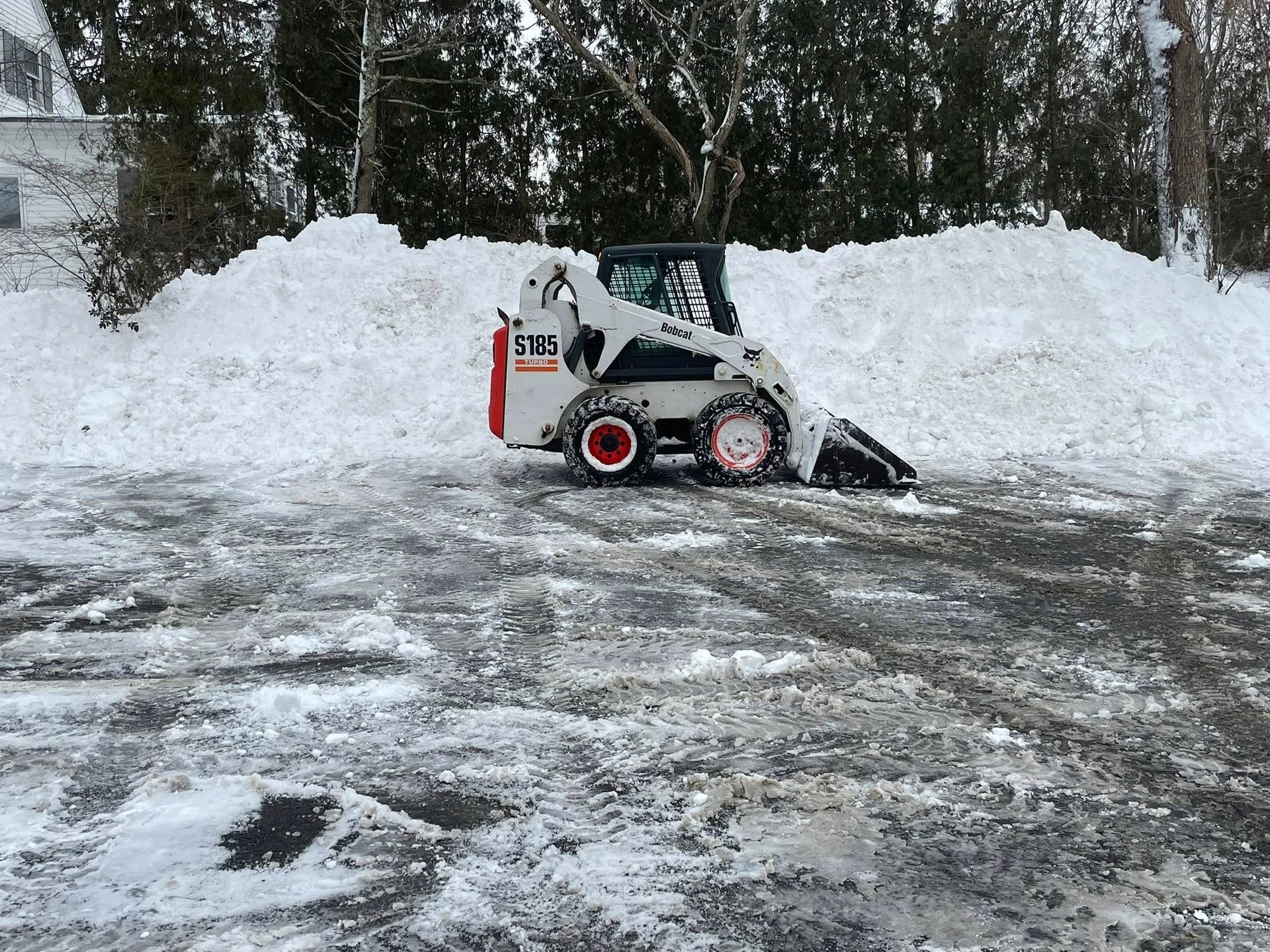 Bobcat skid steer plowing snow in a residential driveway, winter scene.