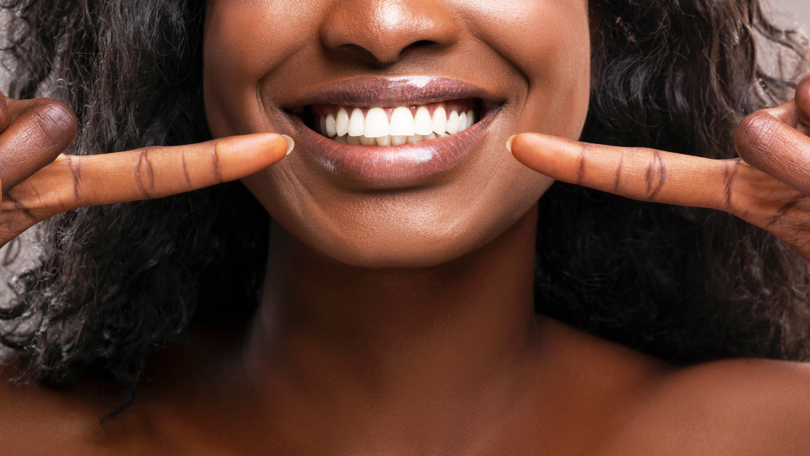 A woman is smiling and pointing at her teeth with her fingers.