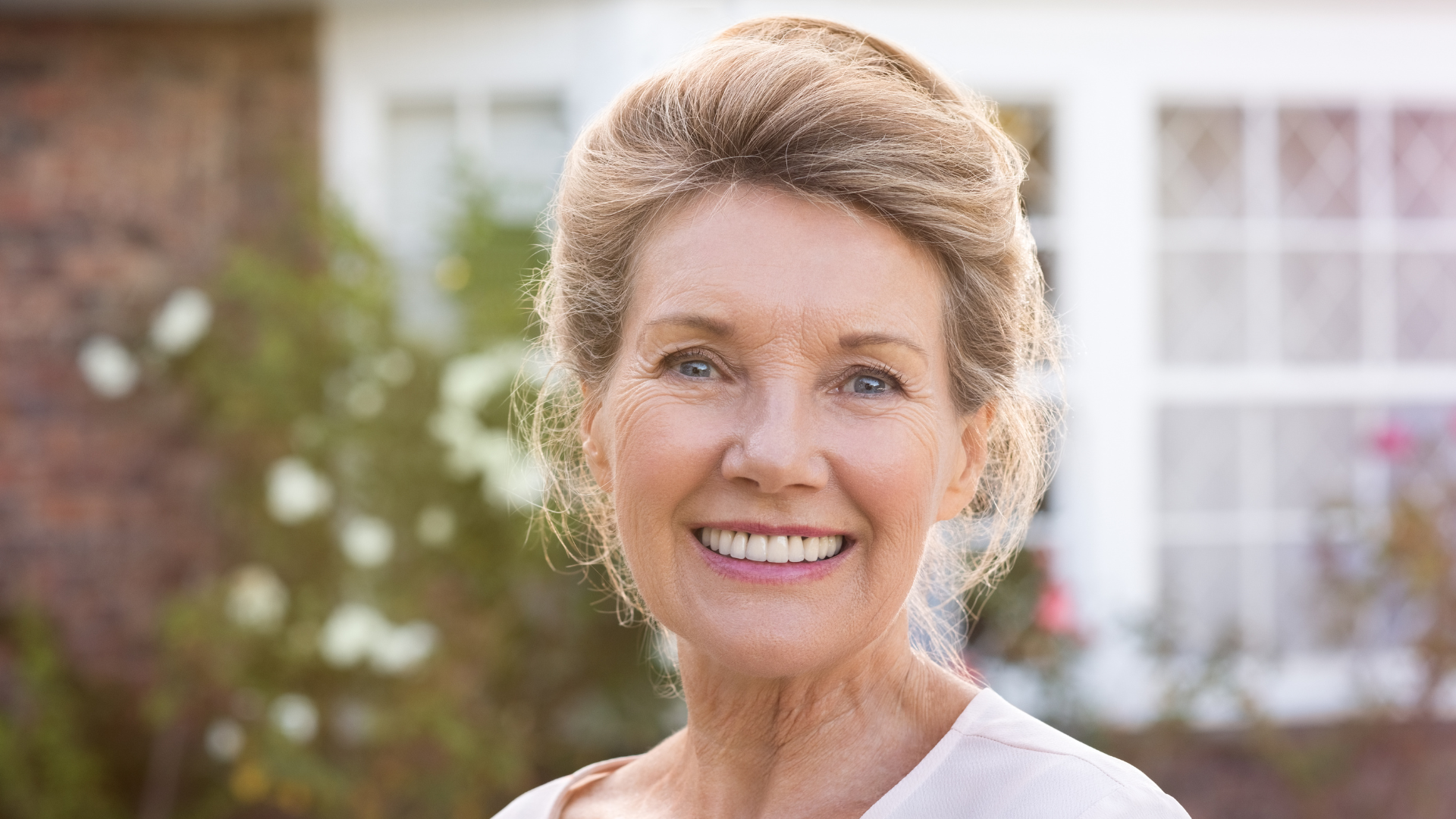 An older woman is smiling in front of a house.