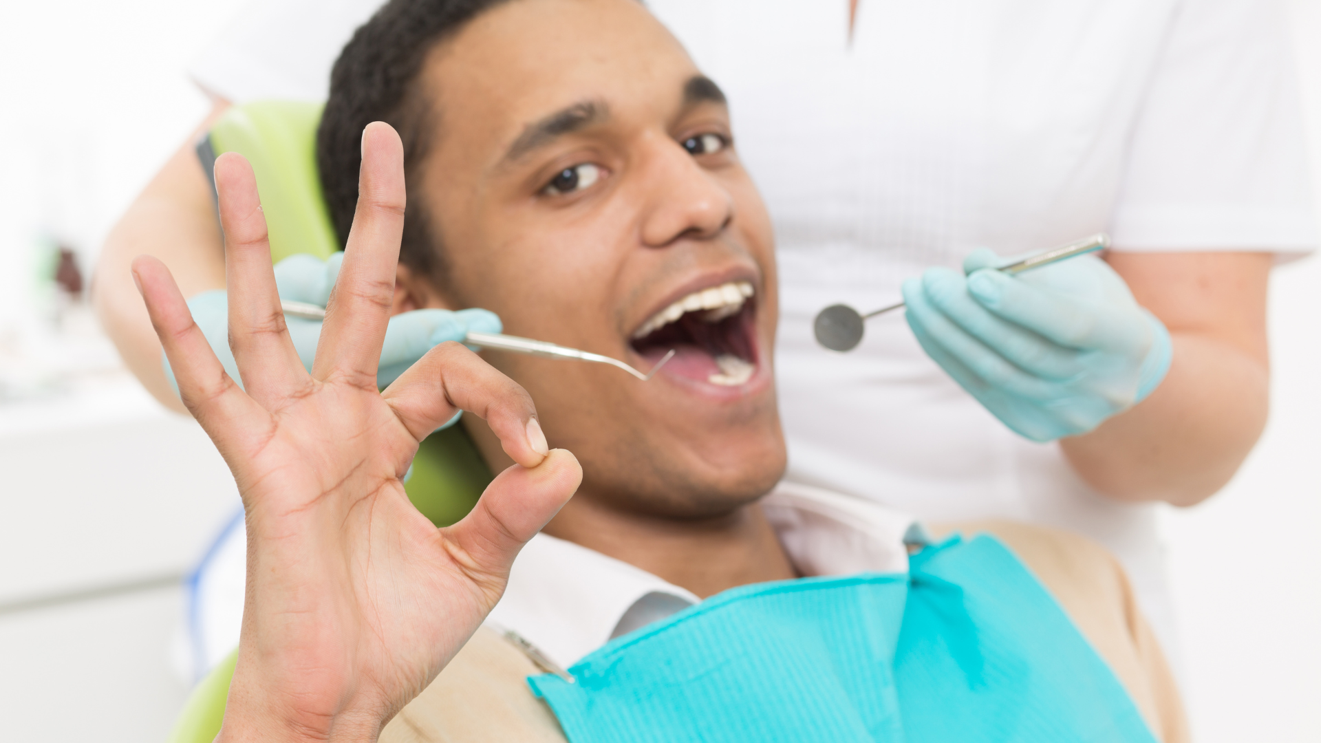 A man is sitting in a dental chair giving an okay sign.