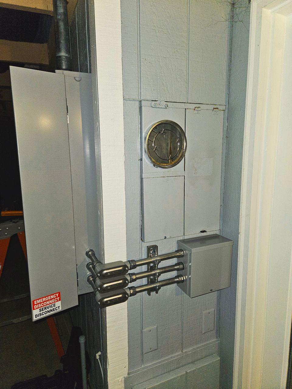 Electrical panel on a concrete wall, with conduit and meter box. Gray and silver components.