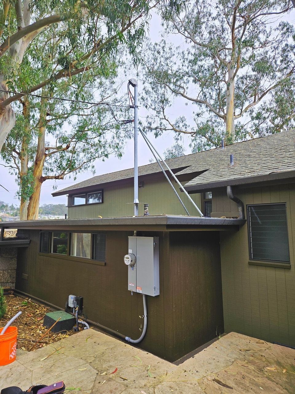 Exterior view of a house with electrical equipment on the side and a tall pole structure extending upwards.