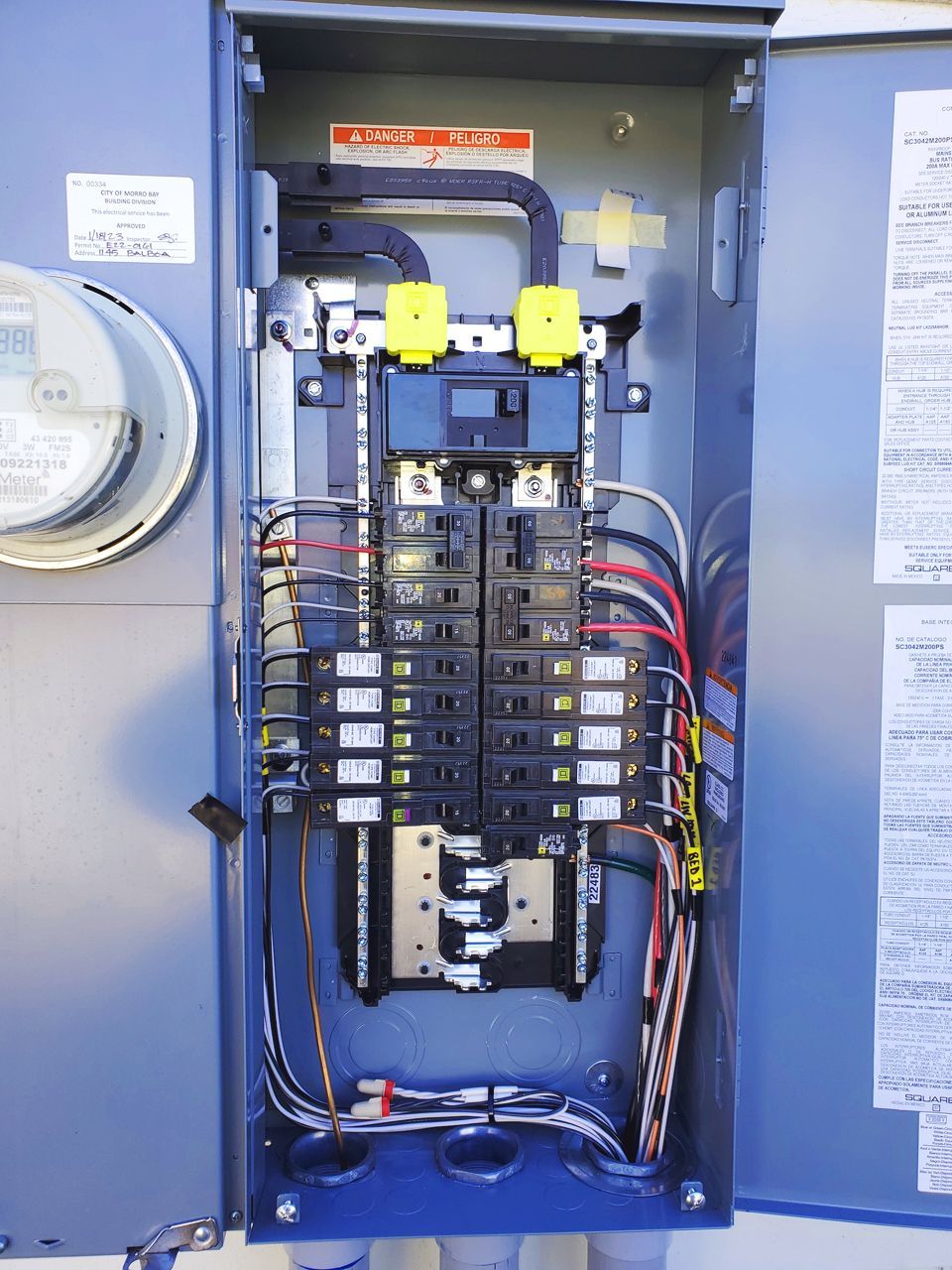 Open electrical panel with circuit breakers, wires, and labels.