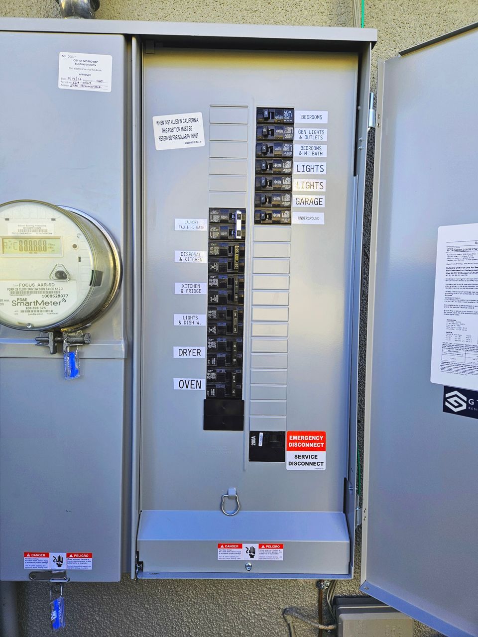Outdoor electrical panel with open door, labels, and circuit breakers. Meter visible on the left side.