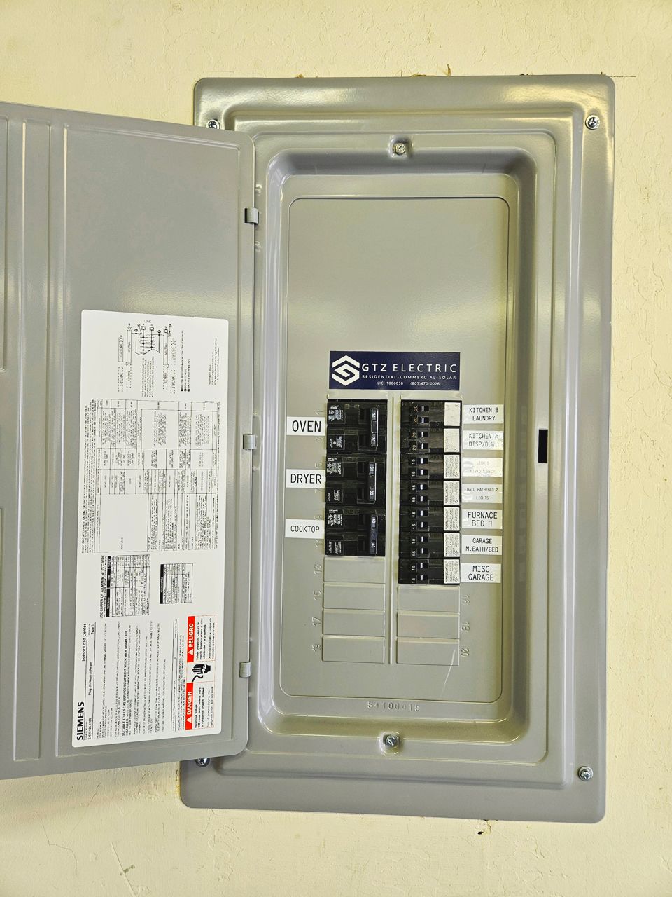 Open electrical panel with circuit breakers. Gray box mounted on a cream-colored wall.