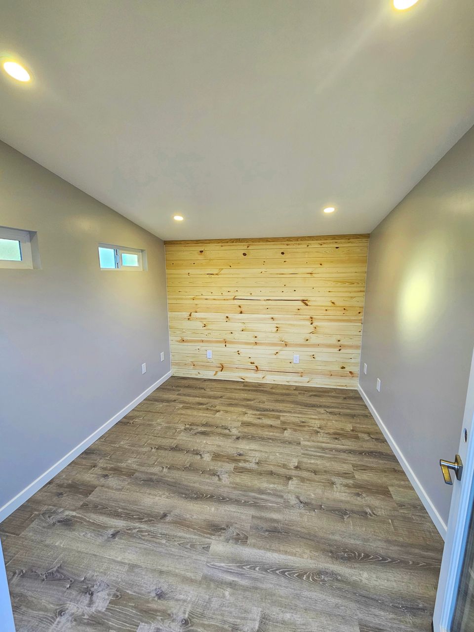 Empty room with wood accent wall, gray walls, light-colored floor, and recessed lighting.
