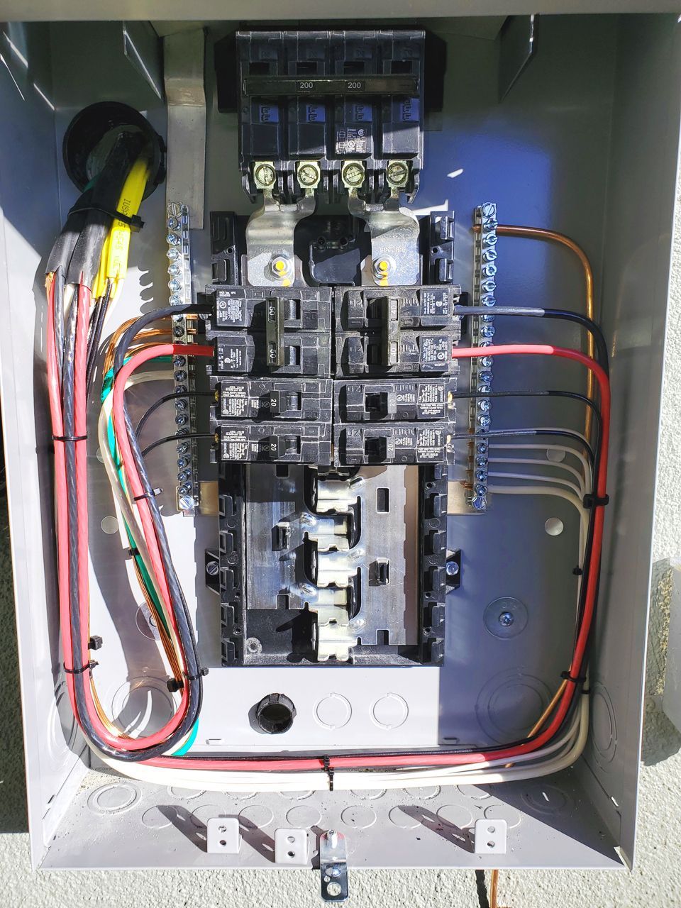 Electrical panel with wires and circuit breakers. Gray metal box, various colored wires.