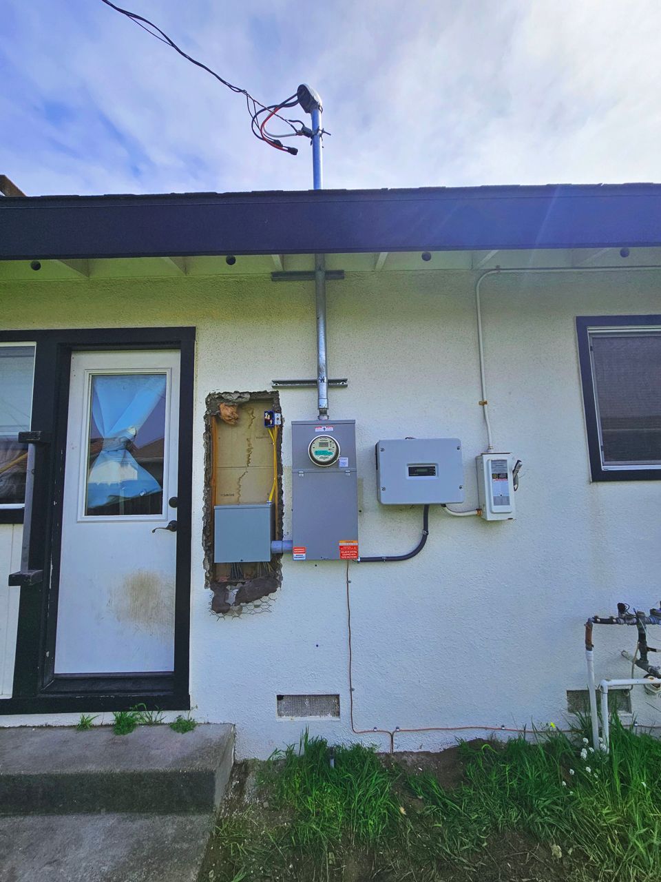 Exterior wall of a house with solar panel equipment: electric meter, inverter, and conduit.