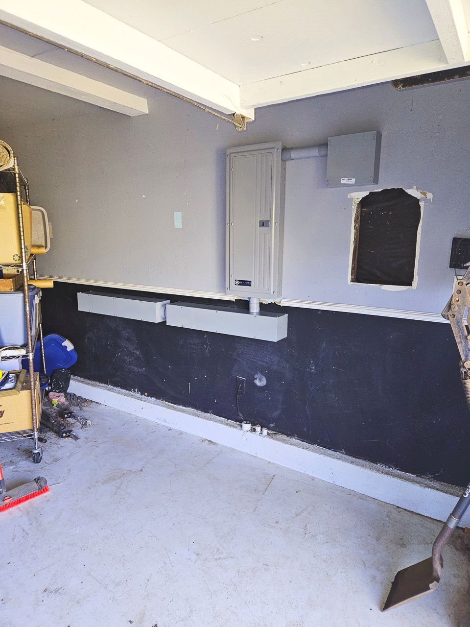 Garage interior, gray walls, electrical panel, dark bottom section, damaged wall, white trim.