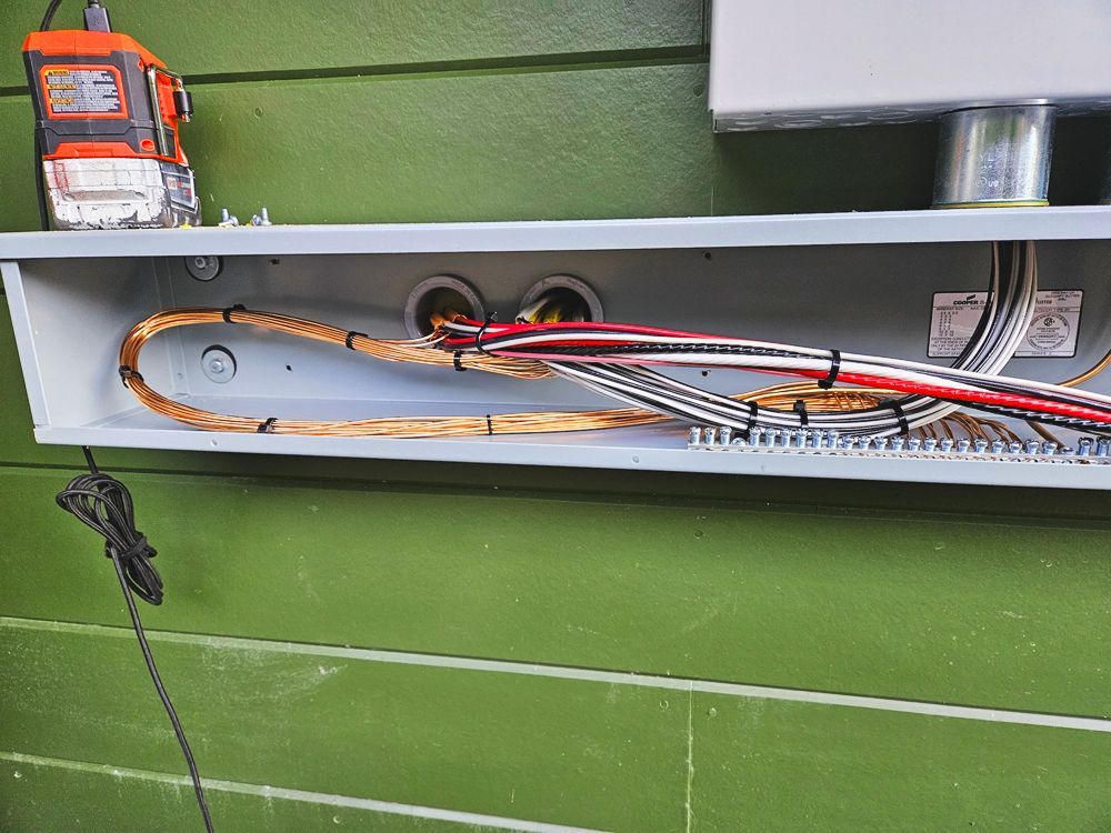Electrical cables and conduit in a metal box on a green wall. A level rests on top.