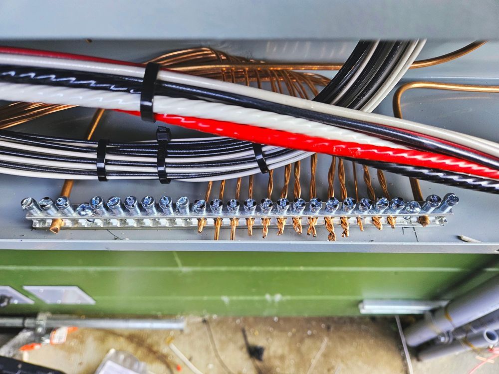 Wiring and cables connected to a grounding bar inside an electrical enclosure.