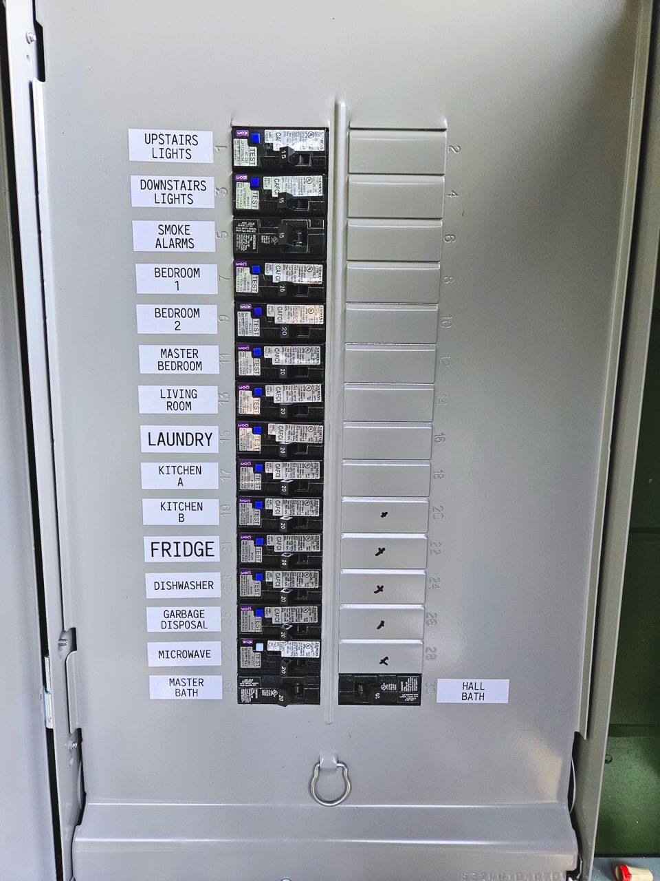 Electrical panel with labeled circuit breakers in a light gray metal cabinet.