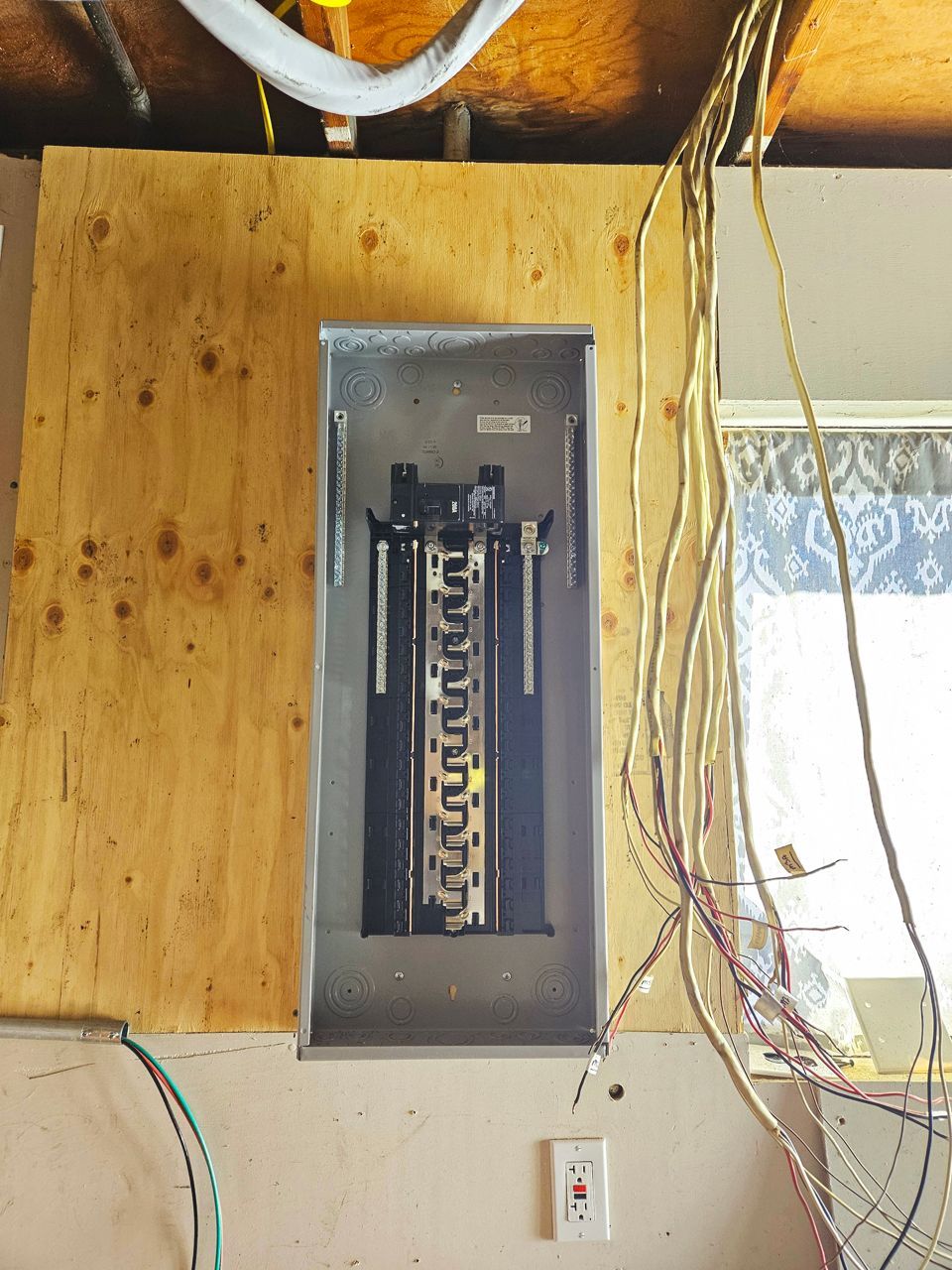 Electrical panel installed on a wooden board; wires and an electrical outlet visible.