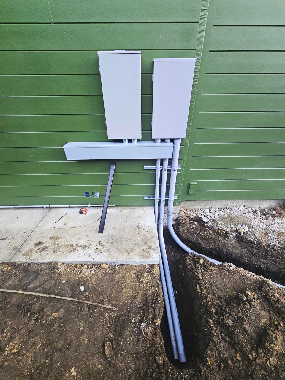 Electrical boxes and conduit on a green building with dirt trench, construction.