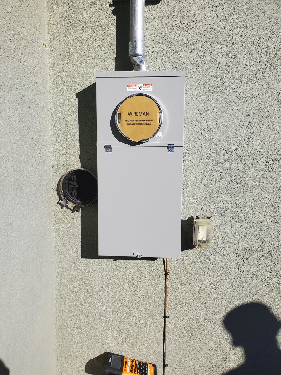 Electrical meter box on a stucco wall with conduit and grounding wire.