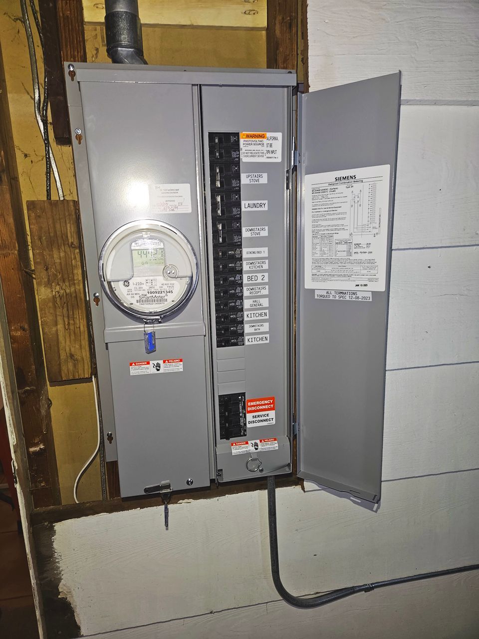 Gray electrical panel with open door, breakers visible. Meter and wiring present.