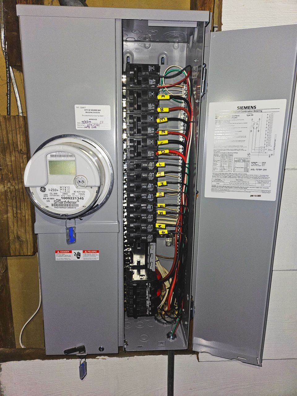 Electrical panel with open door, showing breakers, wires, and meter.